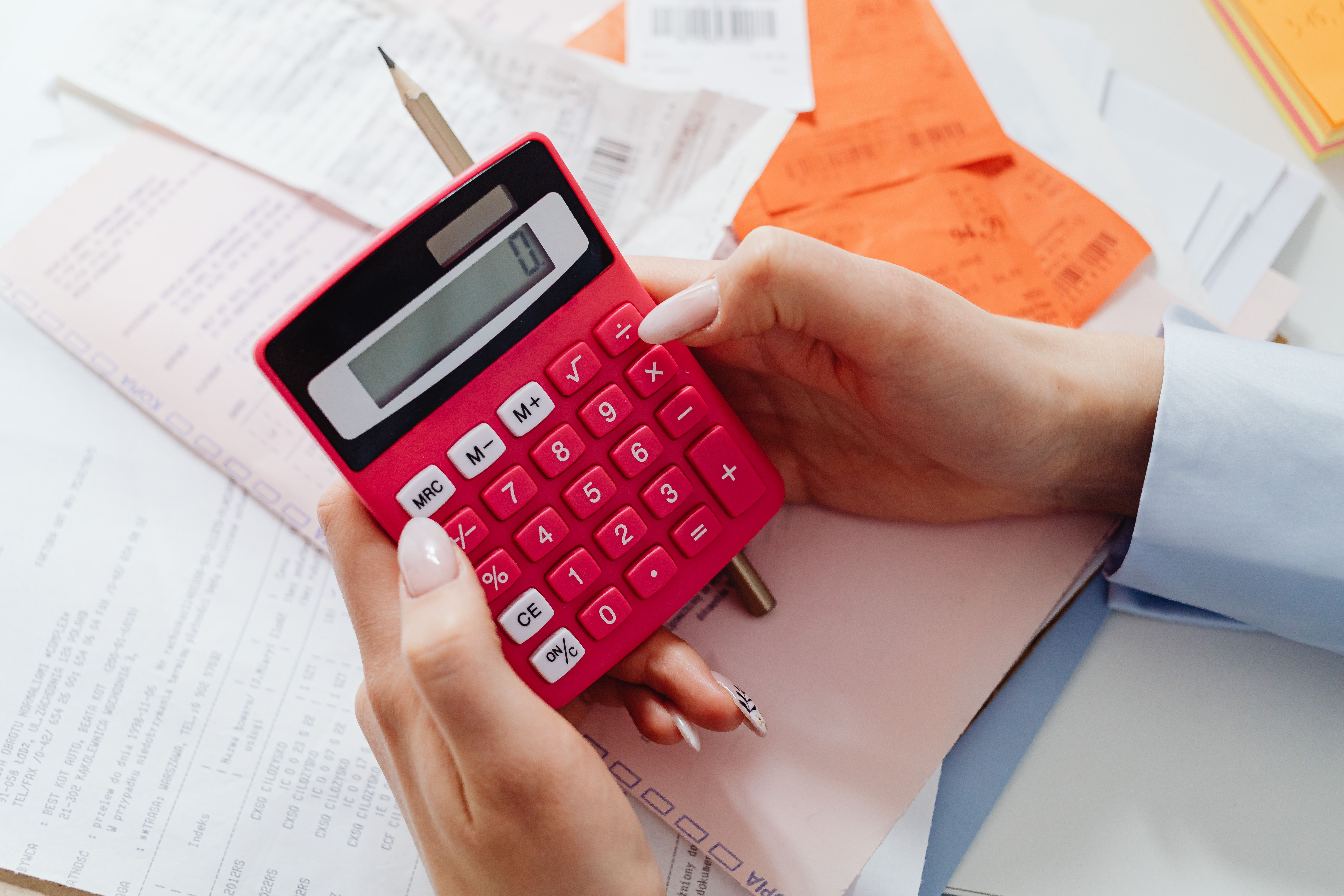 Person calculating NOI using a red calculator